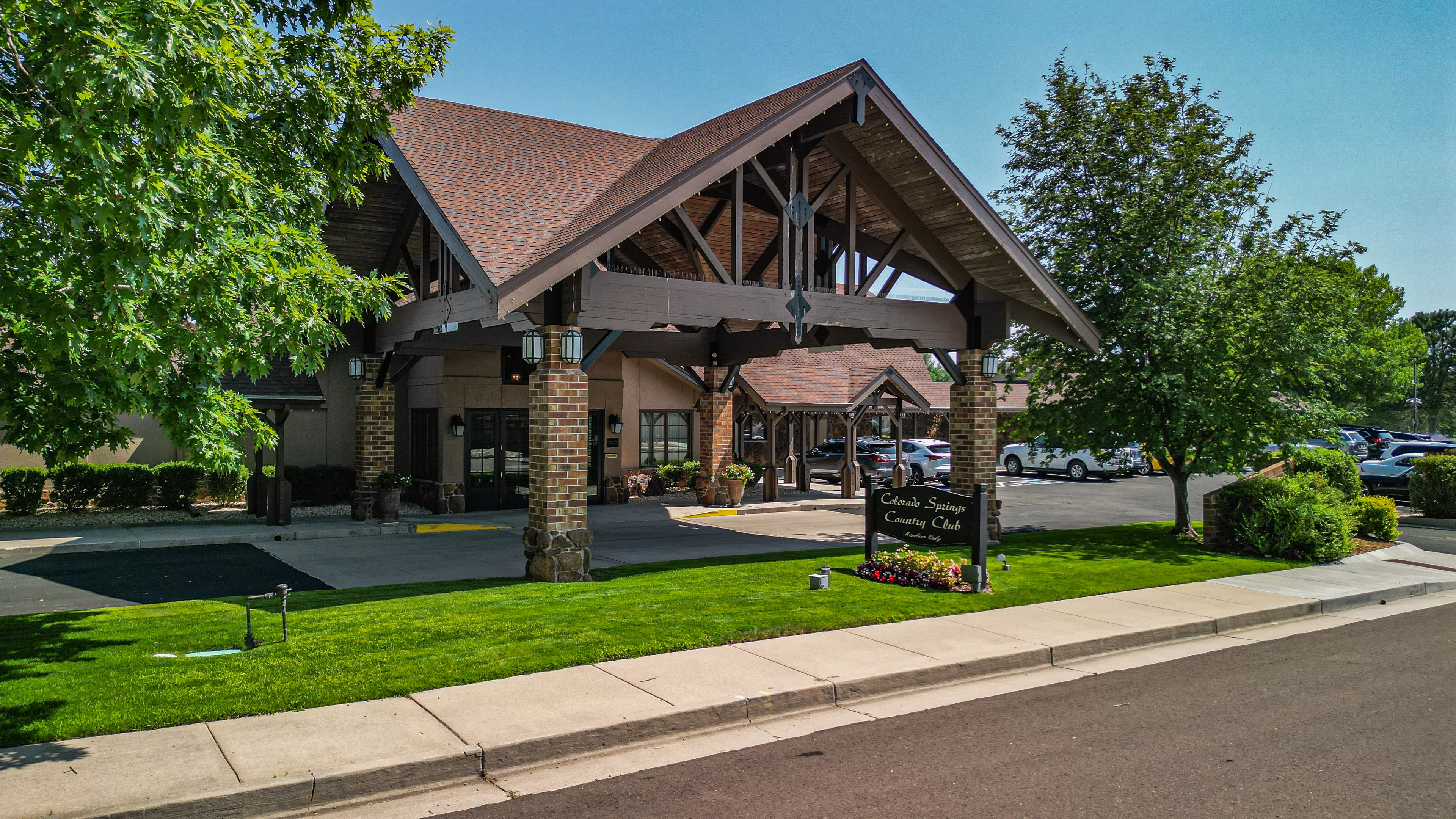 Timber-framed entrance of Colorado Springs Country Club with brick pillars and a green lawn.