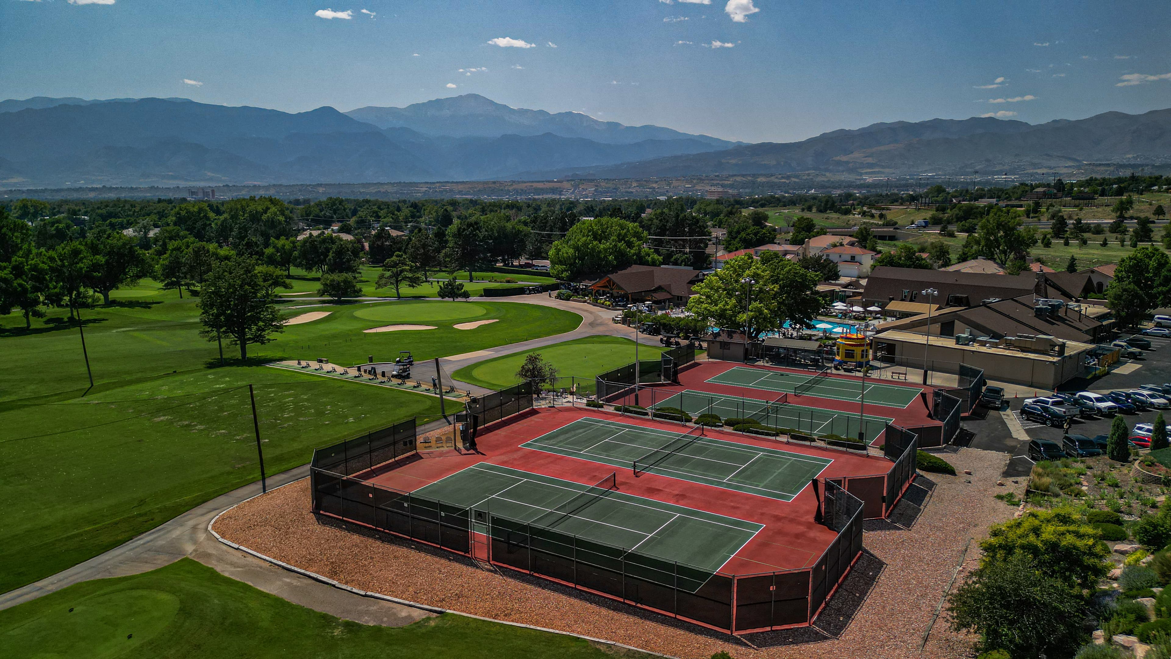 Aerial view of tennis courts and a golf course with a scenic mountain backdrop.