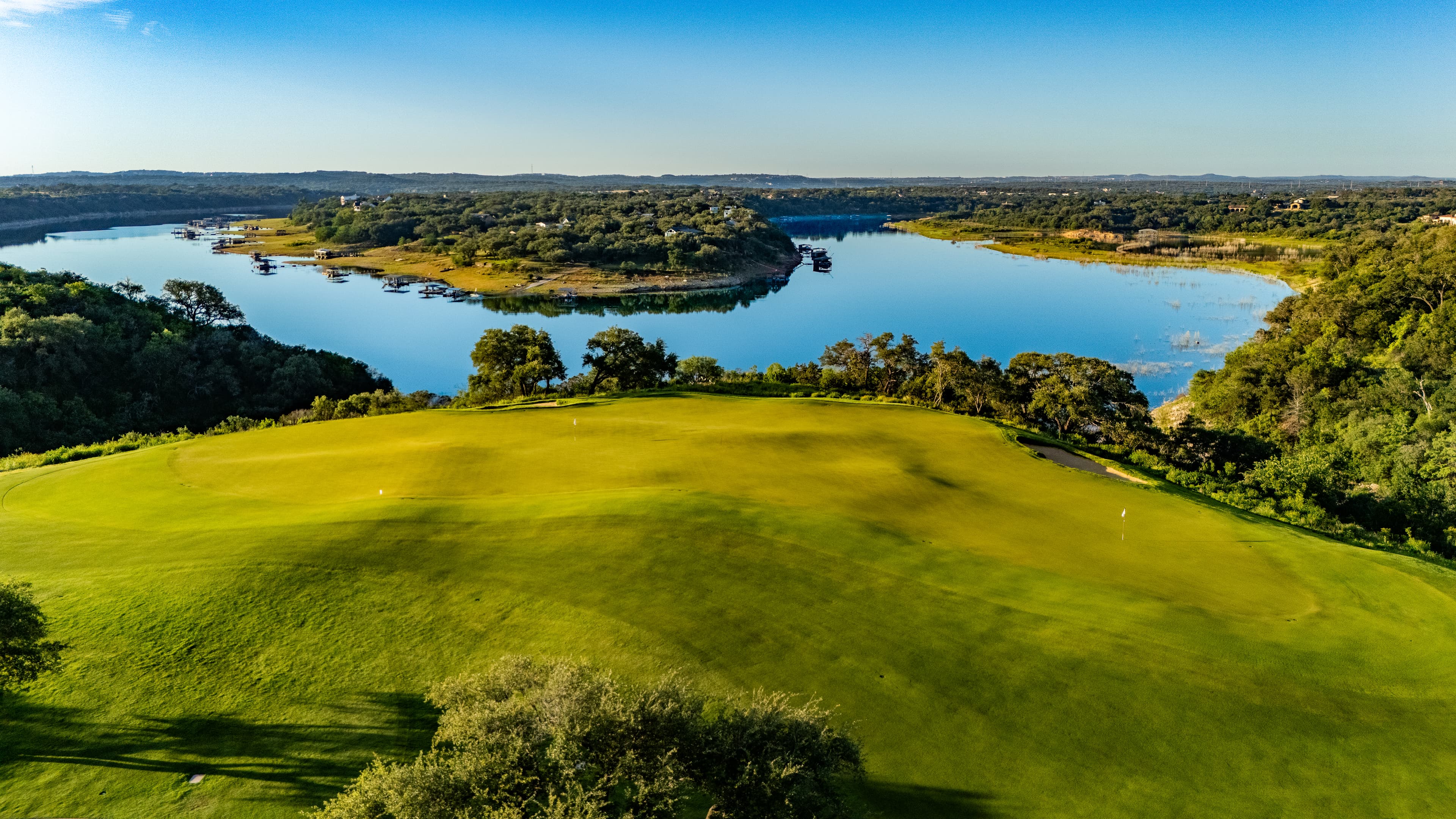 Lush green golf course green overlooking a calm blue lake surrounded by dense trees.