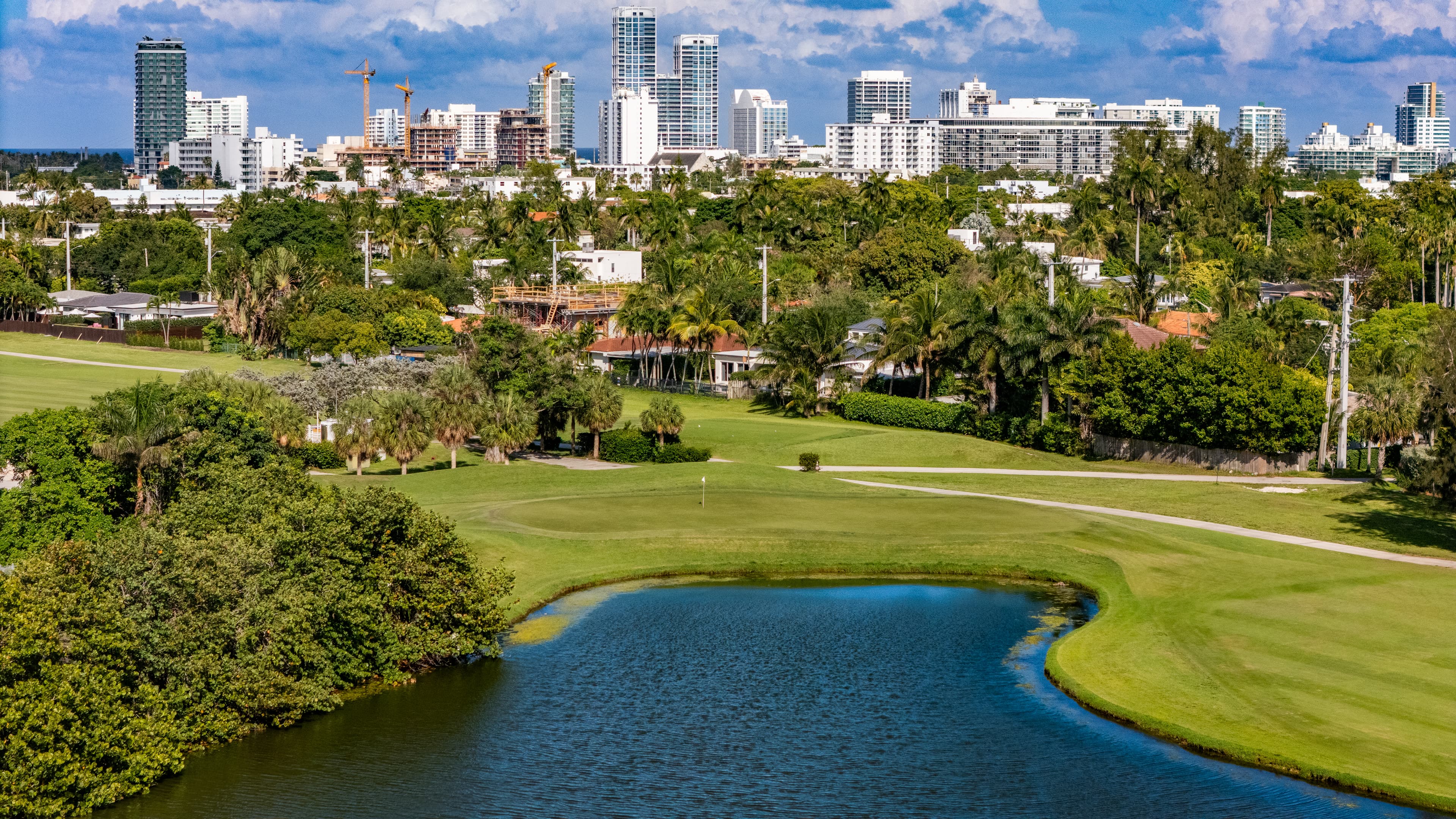 Lush green golf course with a pond in front of a modern city skyline.
